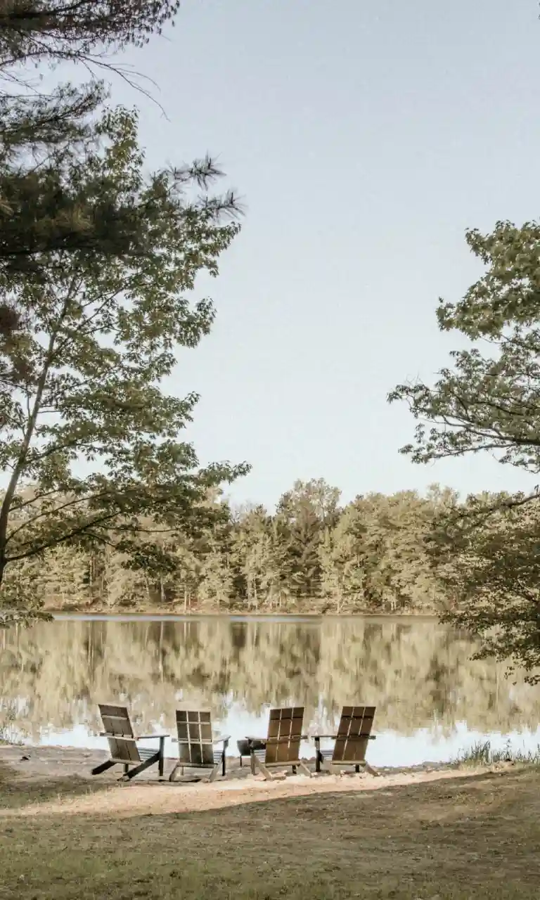 Lakeside view with three chairs and canoes, perfect for a relaxing getaway.